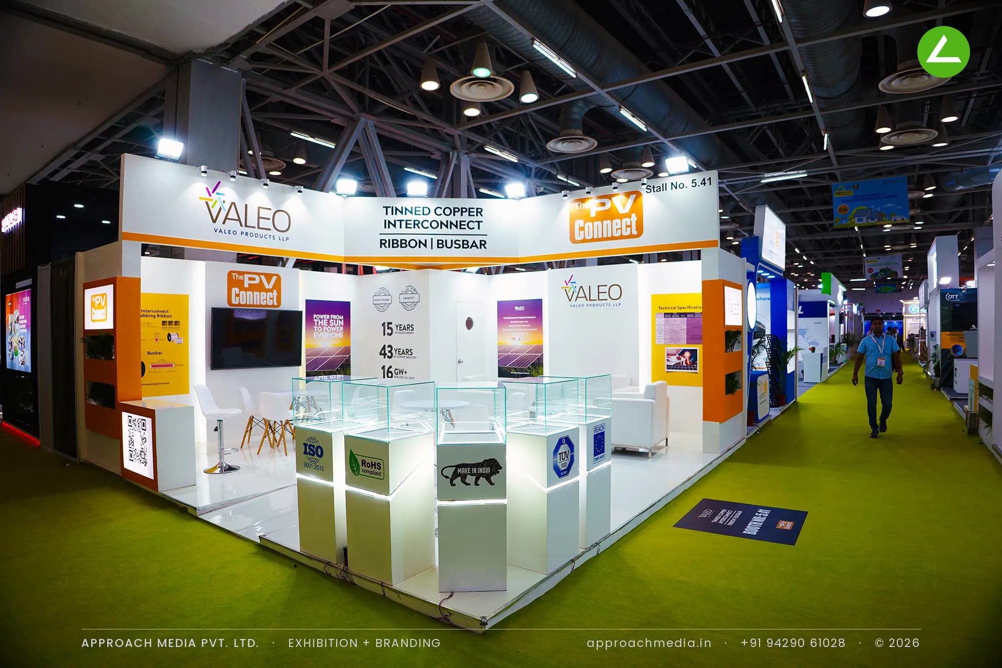 Lit glass vitrines step across the open corner of Valeo's stall, with orange laminate returns and backlit panels behind.