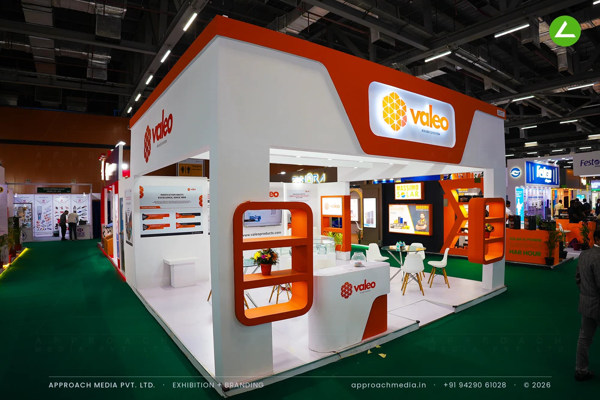 White and orange Valeo exhibition stall design at REI Expo Chennai, backlit logo fascia over an open corner meeting area