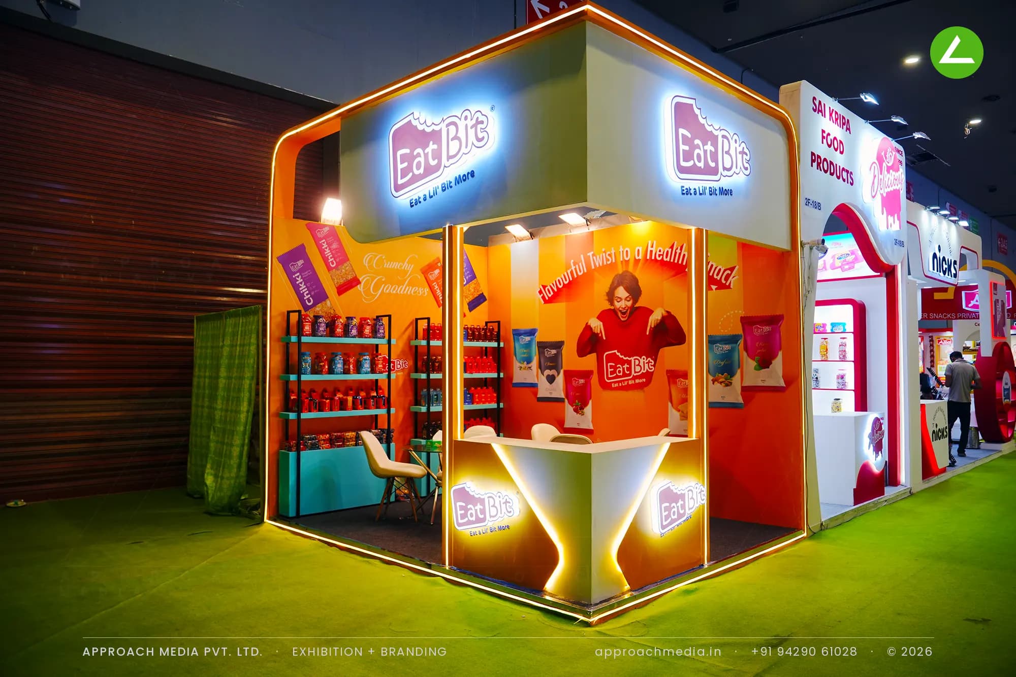 Eat Bit exhibition stall design at Aahar New Delhi with orange graphic walls, a neon-outlined portal and stocked snack racks