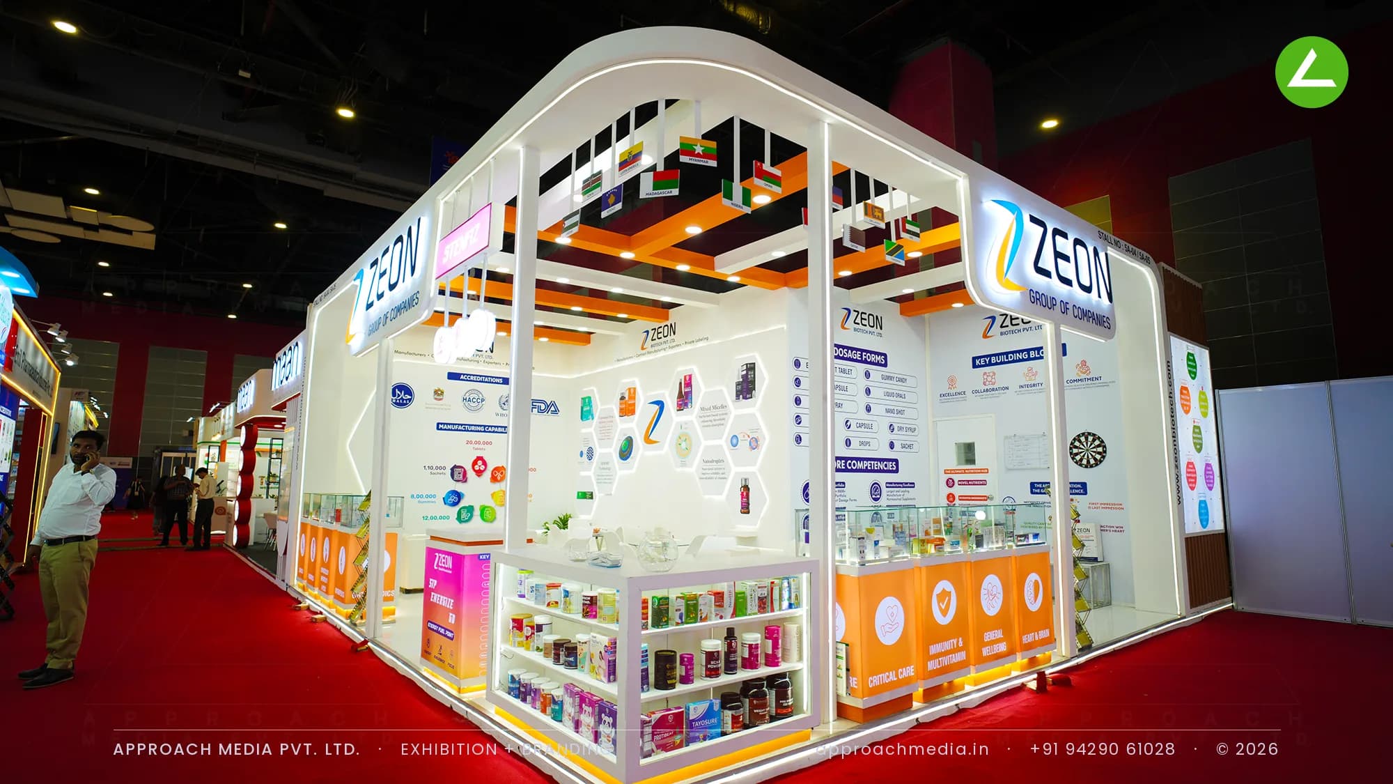 Zeon Group's 44 sqm two-side-open exhibition stall at iPHEX 2026, Bharat Mandapam, with a white portal and an orange ceiling grid hung with country flags