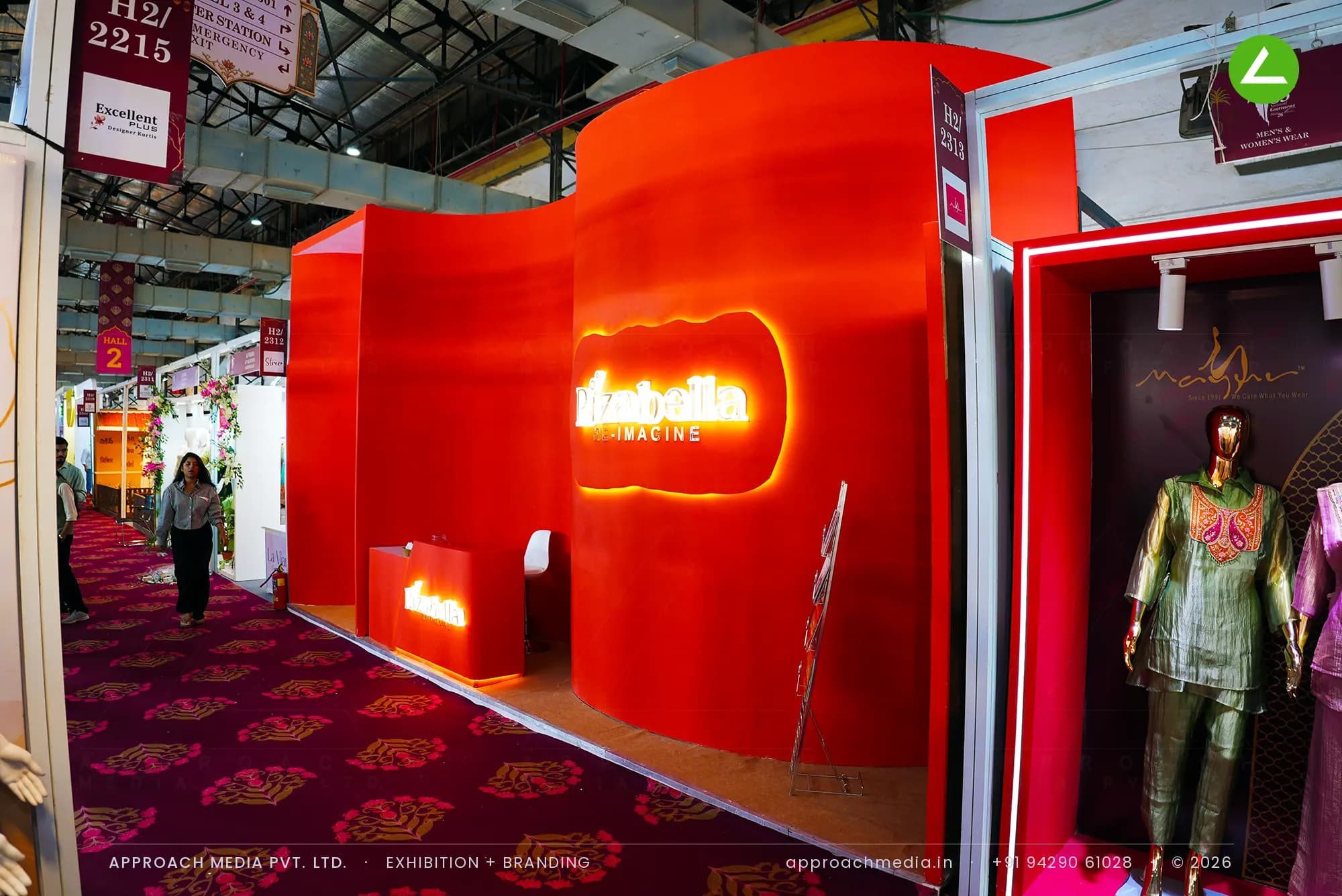 Curved red frontage with halo-lit logo — exhibition stall design at National Garment Fair Mumbai for Rizabella